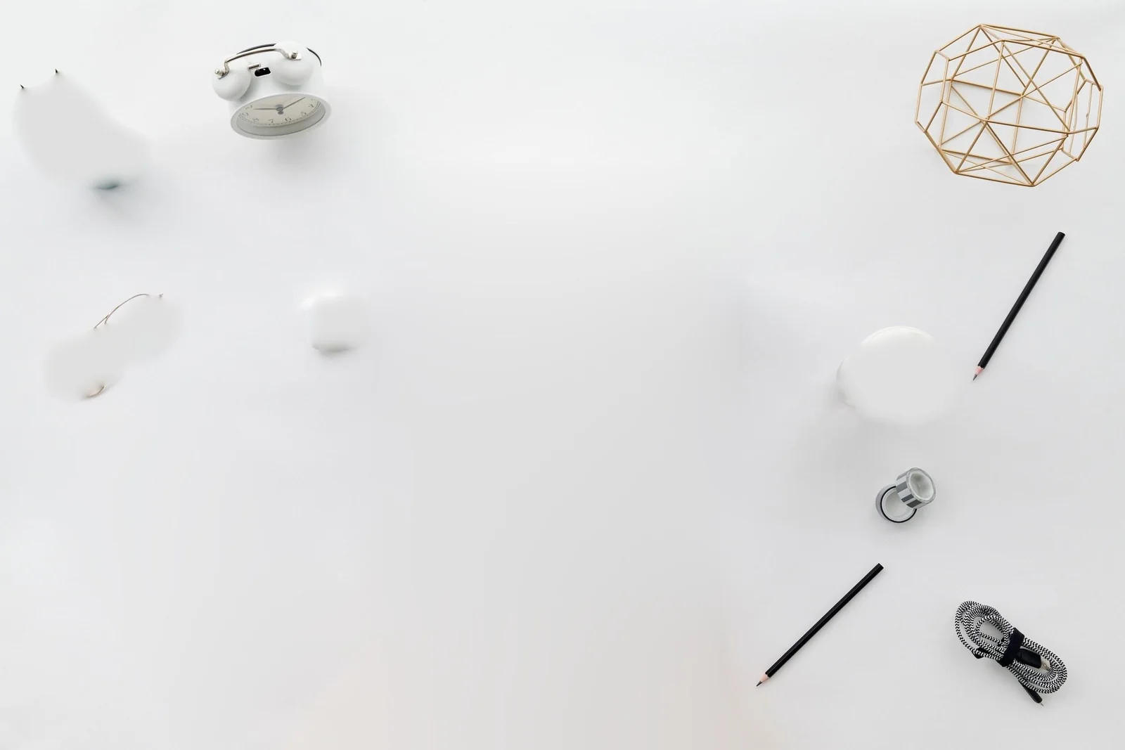 Overhead photo of a white desk with an alarm clock, a small plant, glasses, a coffee cup, pencils, and a gold desk ornament.